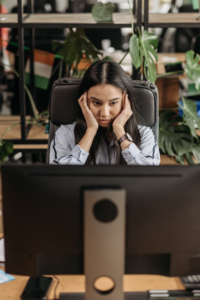 Woman looking tired and stressed while working on computer at office desk.